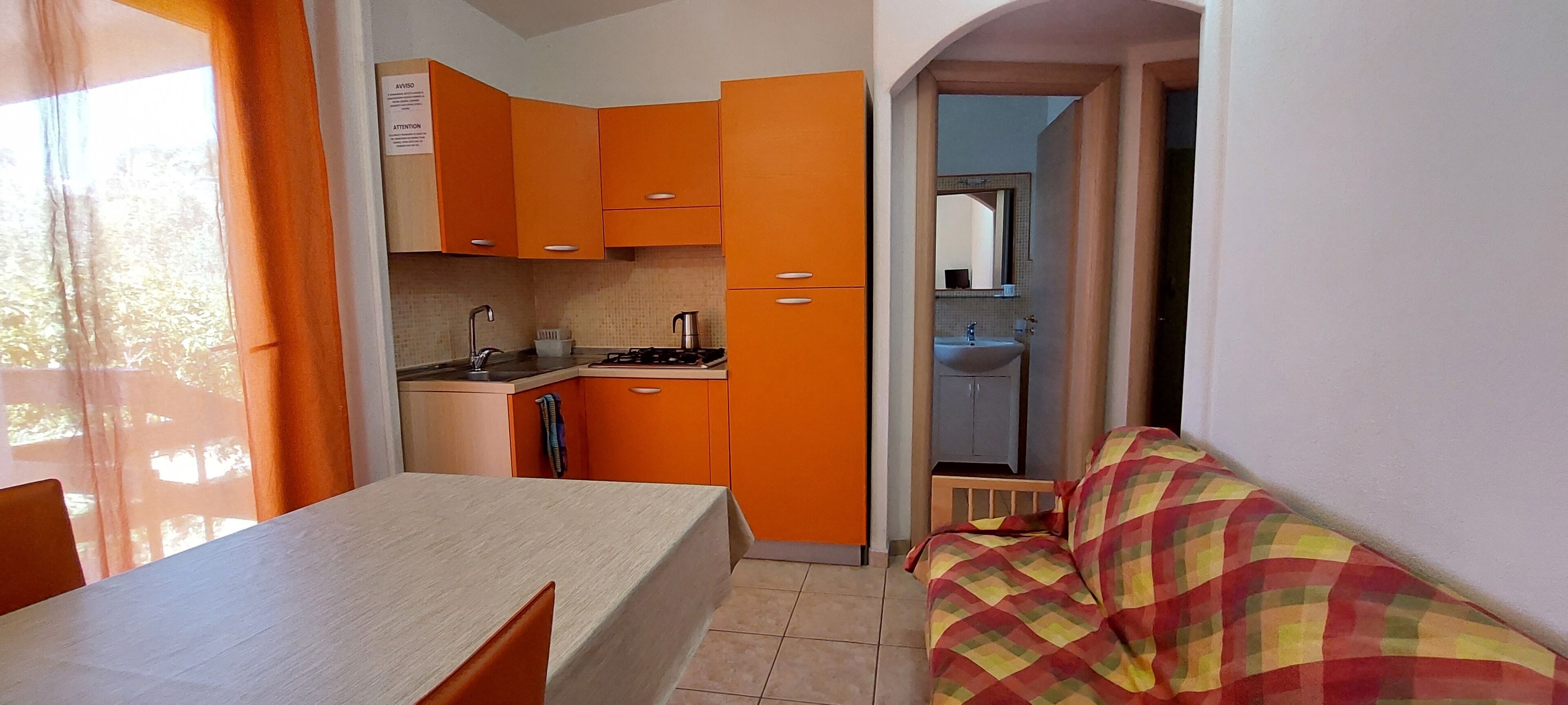 A compact kitchen with orange cabinets, a dining table, and a small kitchenette.