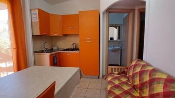 A compact kitchen with orange cabinets, a dining table, and a small kitchenette.
