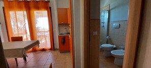 Een kamer met een eettafel, een keuken met een spoelbak en kastjes, en een badkamer met toilet en douche.
