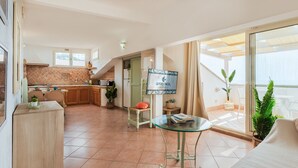 Una sala de estar moderna con una mesa de centro de vidrio, una zona de cocina con comedor, y un balcón con vistas.