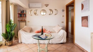Un salón acogedor con un sofá, una mesita con una botella y vasos, una estantería y espejos decorativos con forma de luna en la pared.