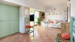 Una sala de estar con un sofá, una mesita de centro y una estantería. Hay una puerta a la izquierda y una ventana a la derecha.