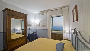 Een hotelkamer met een groot bed, een houten garderobe, een klein tafeltje met een lamp en een raam met gordijnen.