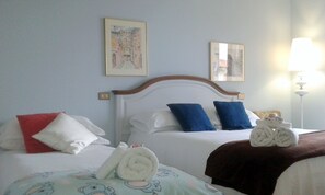 Une chambre d’hôtel avec deux lits, chacun agrémenté de draps blancs et d’oreillers bleus et rouges. Deux œuvres d’art encadrées sont accrochées au mur au-dessus des lits.