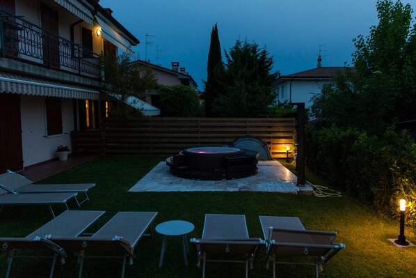 A backyard with a hot tub, lounge chairs, and a wooden fence.