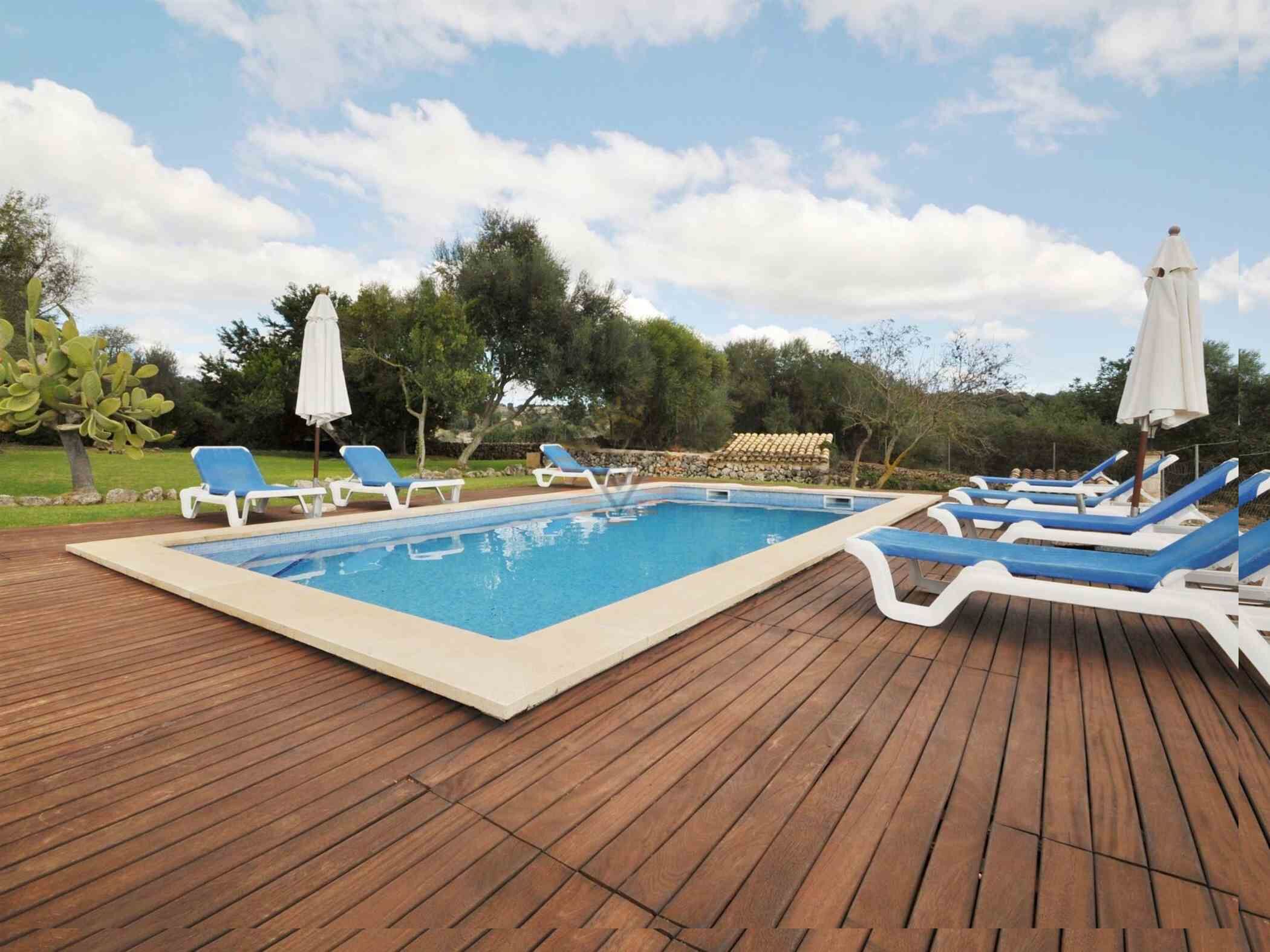 Une piscine rectangulaire, avec des chaises longues bleues et blanches et des parasols, sur une terrasse en bois.