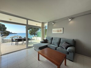 A modern living room with a grey sofa, a wooden coffee table, and a large sliding glass door leading to a balcony with a view of the sea. - Agi Almadraba 2201 Apartamento for rent in Roses Girona. (Roses)