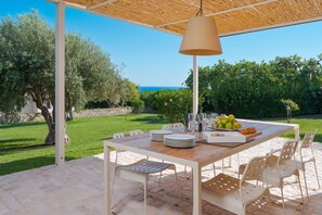 An outdoor patio with a table set for dining, surrounded by chairs, and a hanging lamp. - Beautiful villa with a sea-view terrace and private garden in Scicli. Shared pool - Dicasainsicilia (Scicli)