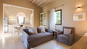 Un salon moderne avec un canapé, un fauteuil et une table à manger. On aperçoit une cuisine au fond, avec un réfrigérateur et des placards.