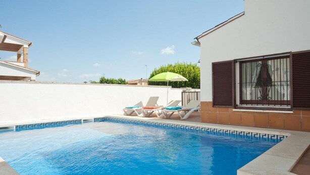 A swimming pool with clear blue water, surrounded by a white wall and a tiled deck. There are lounge chairs and a green umbrella. - Villa with private swimming pool.HUTG-015590 (l'Escala)