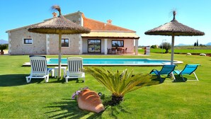 Una casa con piscina, mobiliario exterior y jardín.