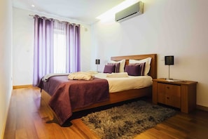 Une chambre à coucher comprenant un lit, une table de chevet, une lampe, un tapis et un appareil de climatisation.