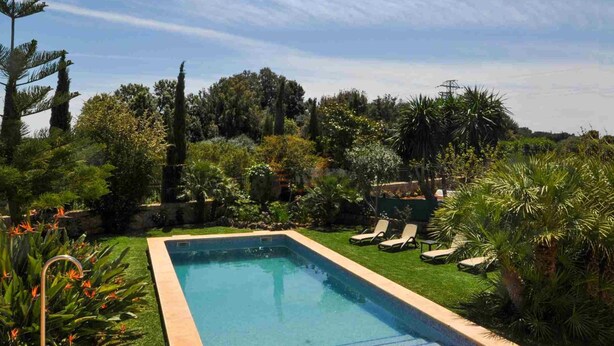 A rectangular swimming pool with a wooden deck edge, surrounded by lush greenery and a clear sky. - Casa Antonio: Rural Charm with Pool (Buger)