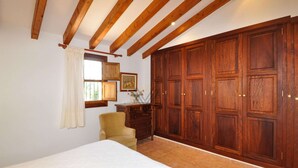 A bedroom with wooden beams, a large wardrobe, a chair, and a bed. - Casa Antonio: Rural Charm with Pool (Buger)