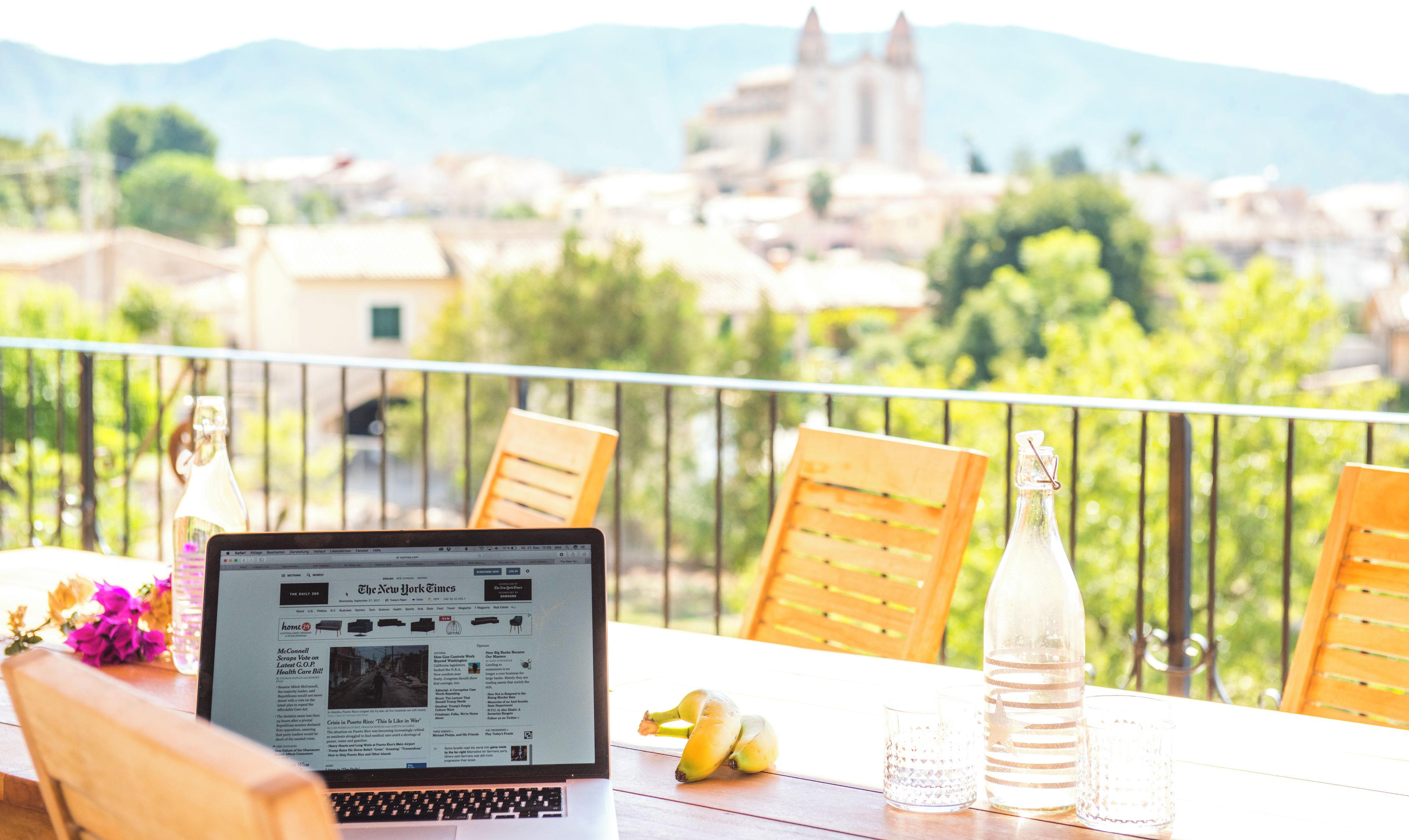 A laptop on a balcony with a view of a historic building and mountains.