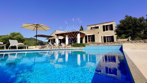 A swimming pool with lounge chairs and umbrellas, a stone building with multiple windows, and a clear blue sky. - Charming Mallorcan house with beautiful views (Son Servera)