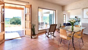 A spacious room with a glass dining table, chairs, and a view of the outdoors. - Charming Mallorcan house with beautiful views (Son Servera)