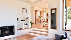 A modern living room with a fireplace, a sofa, a glass coffee table, and a dining area with chairs and a table. - Charming Mallorcan house with beautiful views (Son Servera)