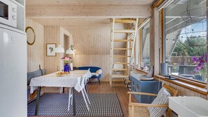 A cozy kitchen with wooden walls, a dining table with chairs, a blue chair, a small table with a vase of flowers, and a window with a view of greenery. - 3 bedroom gorgeous home in Rudkøbing (Rudkøbing)