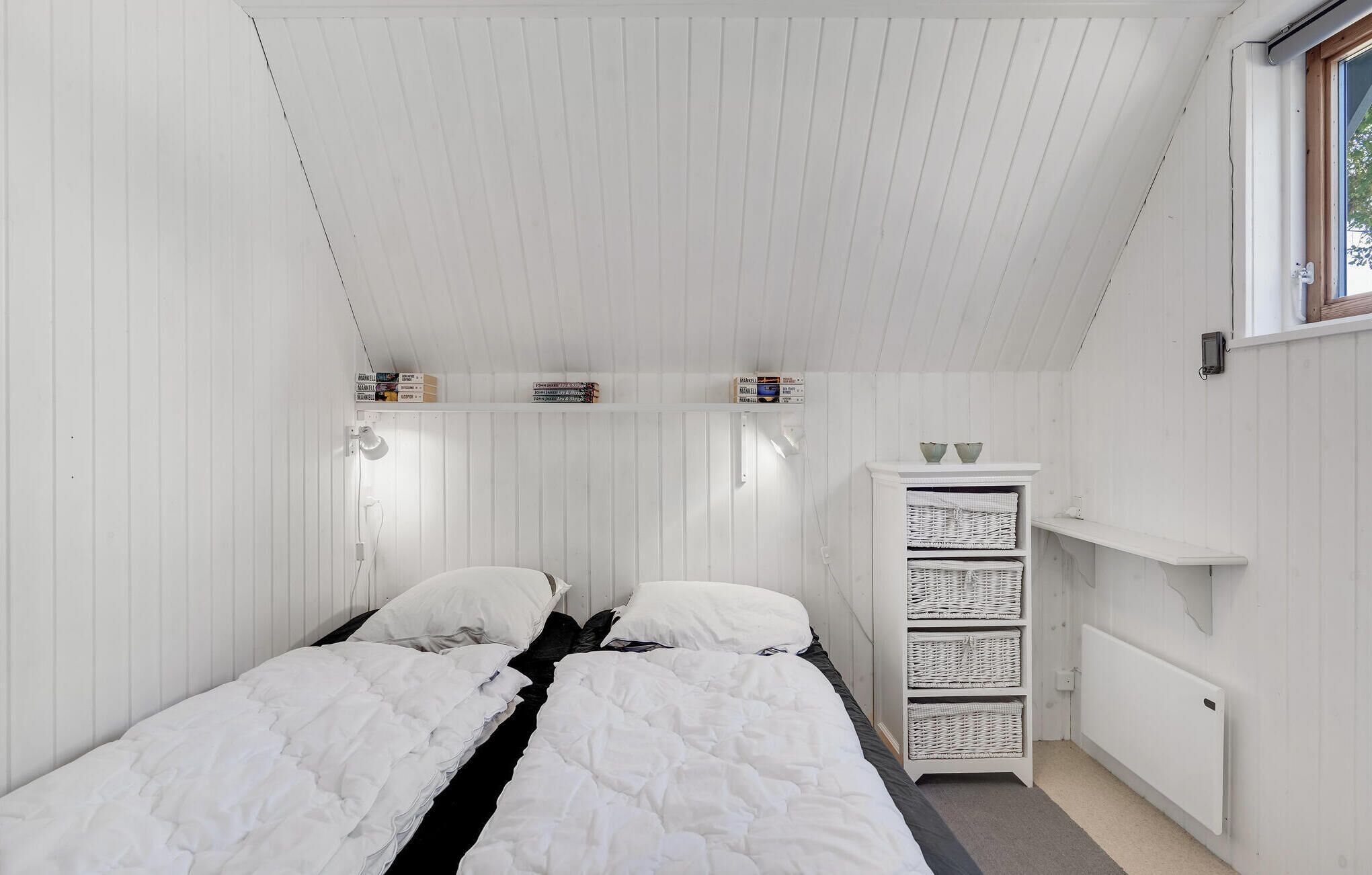 Een kleine kamer met witte muren, twee bedden, een radiator en een plank met manden.