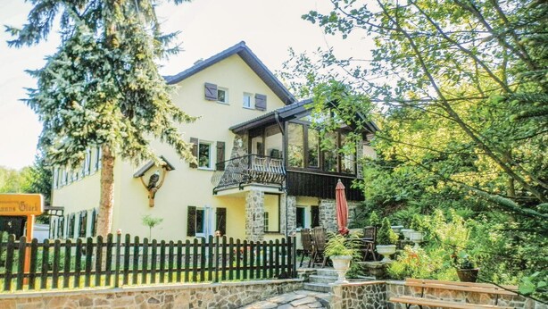 Een huis met twee verdiepingen, een stenen gevel, een balkon en een pad van steen dat naar een houten bankje leidt.