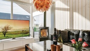 A modern living room with a large TV, a fireplace, a sofa, and a table with a bottle and glasses. - 4 bedroom nice home in Odder (Odder)