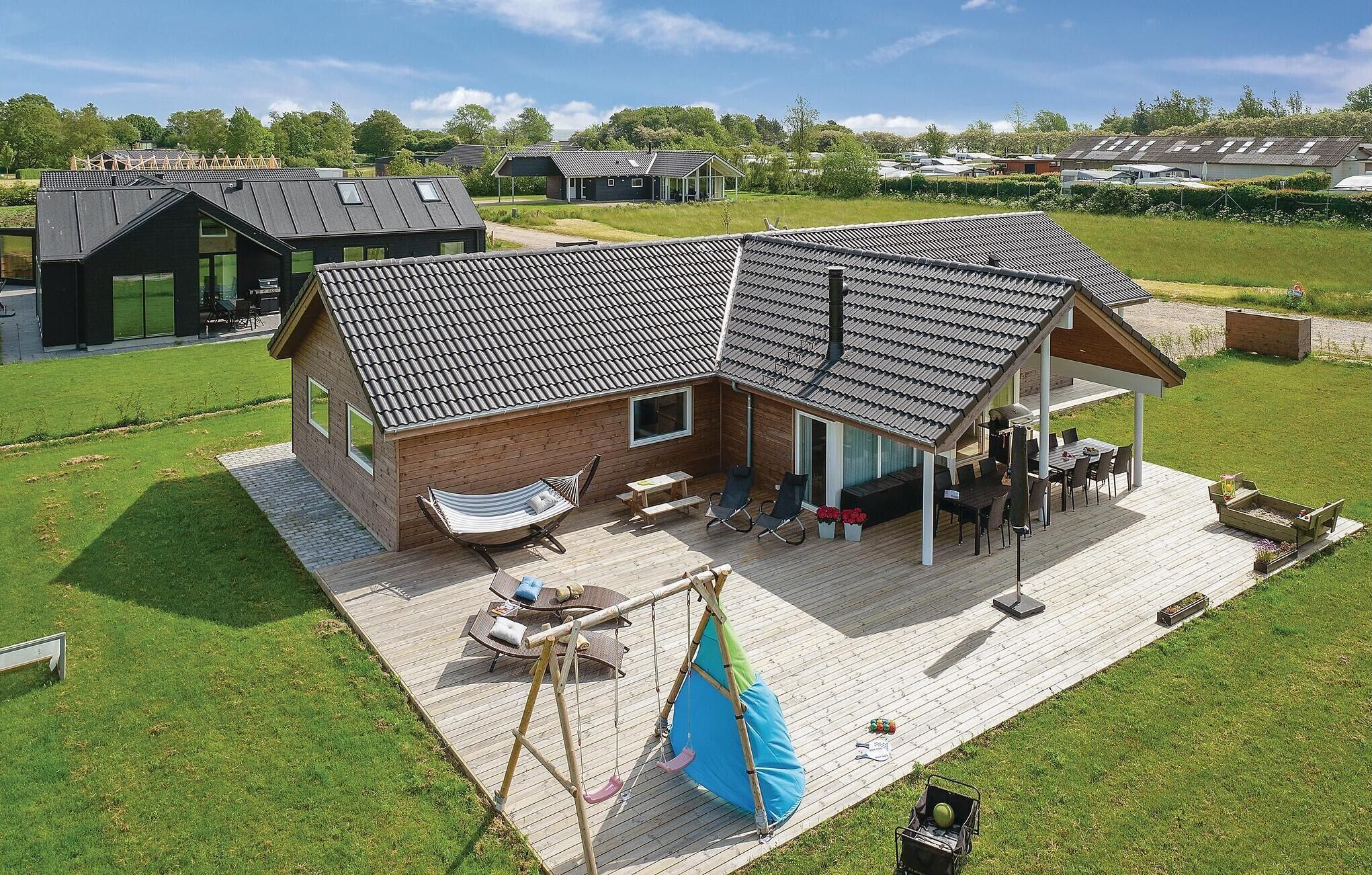 A modern house with a large deck, a hammock, and a swing set.