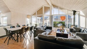 A spacious living area with a large window, a dining table, and several sofas. - 4 bedroom nice home in Odder (Odder)