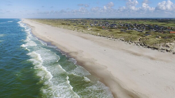 Un paysage côtier avec une plage de sable et une ville en arrière-plan.