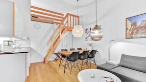 Un appartement moderne comprenant une cuisine, un coin repas et un salon. Il est doté d’un escalier en bois, d’une table à manger avec des chaises, d’un canapé et d’une table basse.