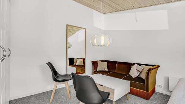 Una habitación moderna con techo de madera, una silla negra, un sofá marrón, un escritorio blanco y un espejo grande.