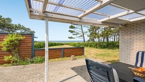 En overdækket terrasse med havudsigt, et træhegn og en murstensmur.