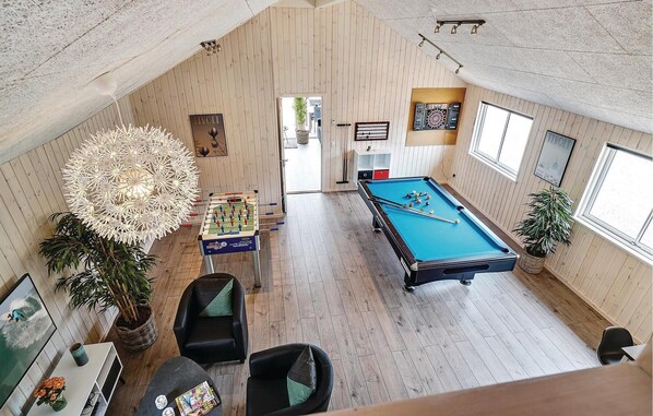 A spacious room with a foosball table, a pool table, and a dartboard. There are two chairs and a table with a vase of flowers.