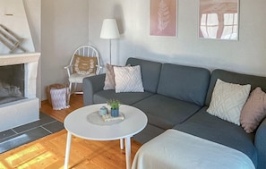 Un salon avec un canapé gris, une table basse blanche, une cheminée et un fauteuil avec des coussins.