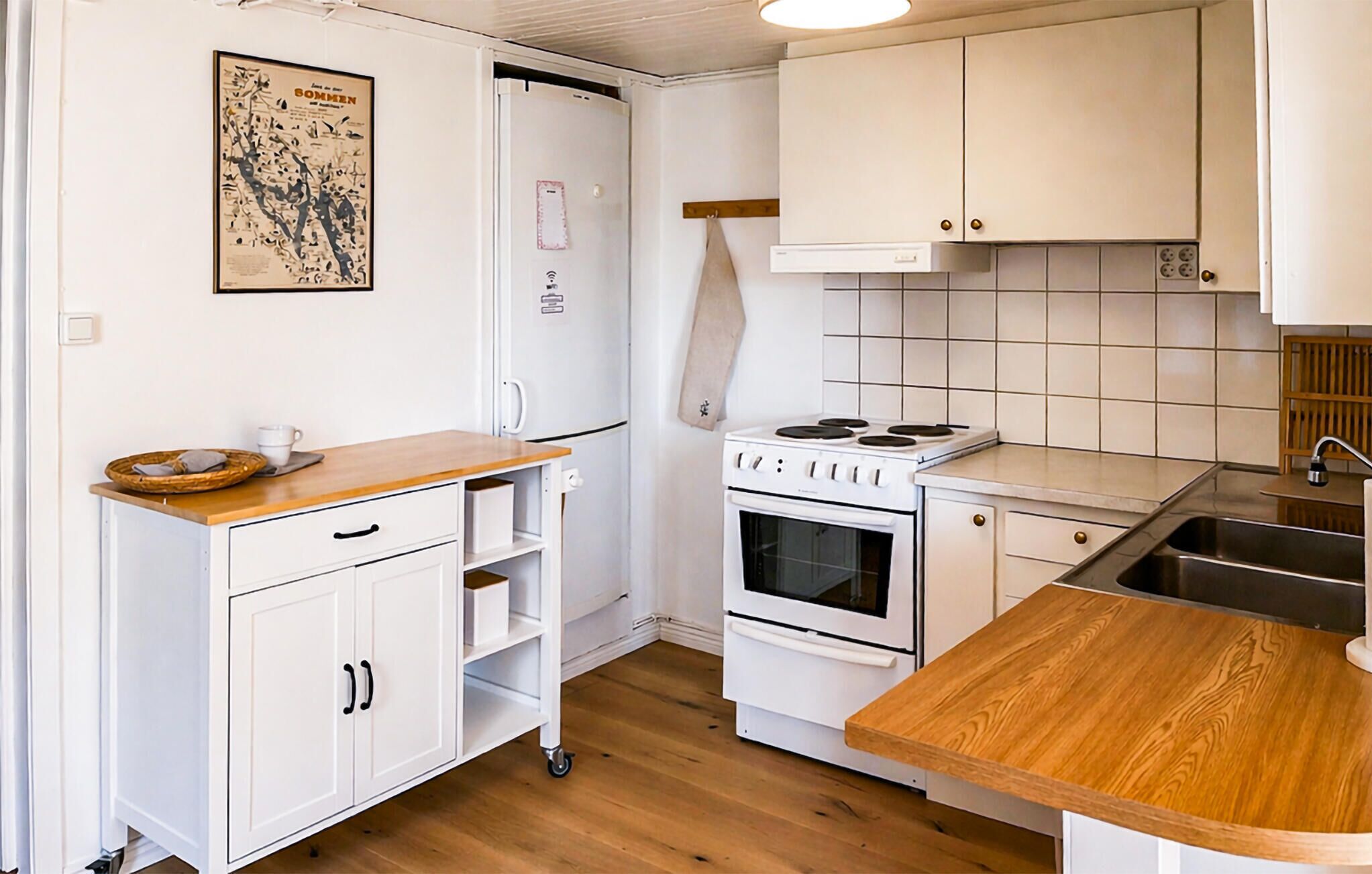 Una cucina compatta con mobili bianchi, un piano di lavoro in legno, un fornello e un frigorifero.