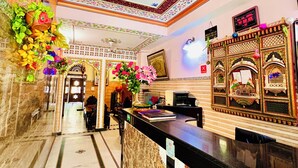 A hotel lobby with a reception desk, a digital clock, and a decorative wall with floral patterns. - Hotel Moon Light Palace Jaipur (Jaipur)