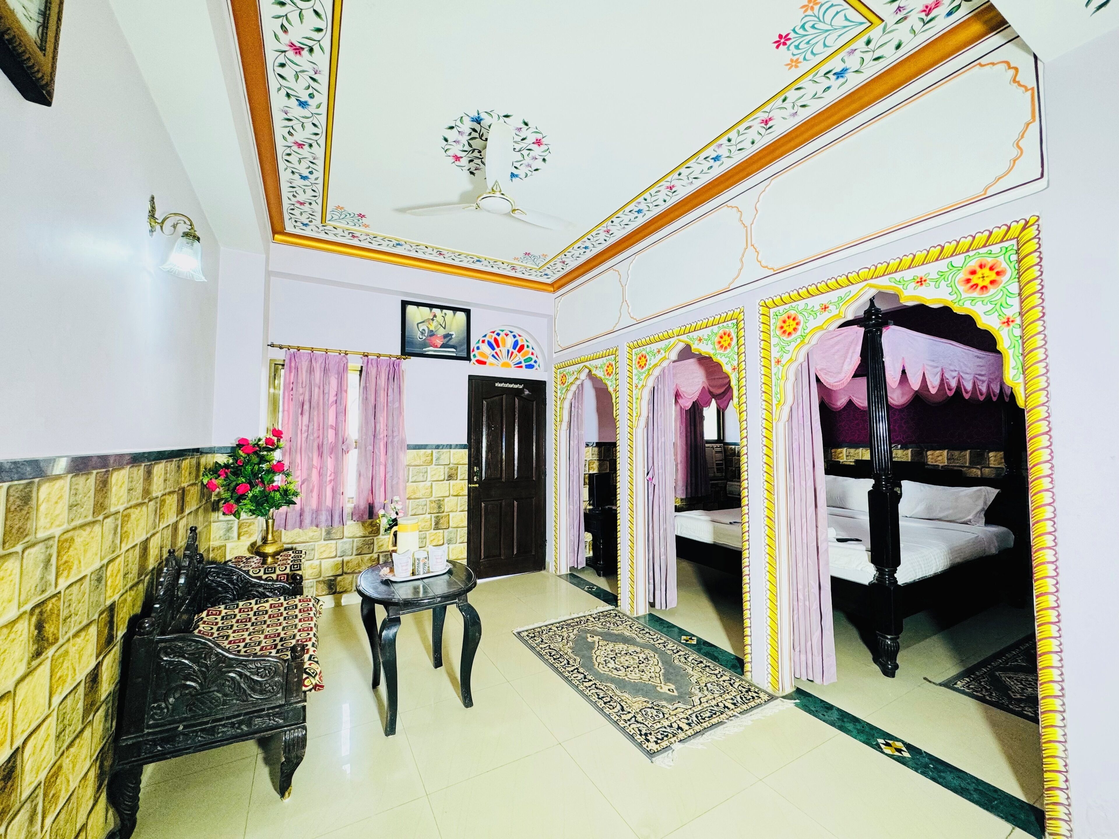 A room with a bed, a small table, a decorative mirror, a door, and a wall with a floral pattern.