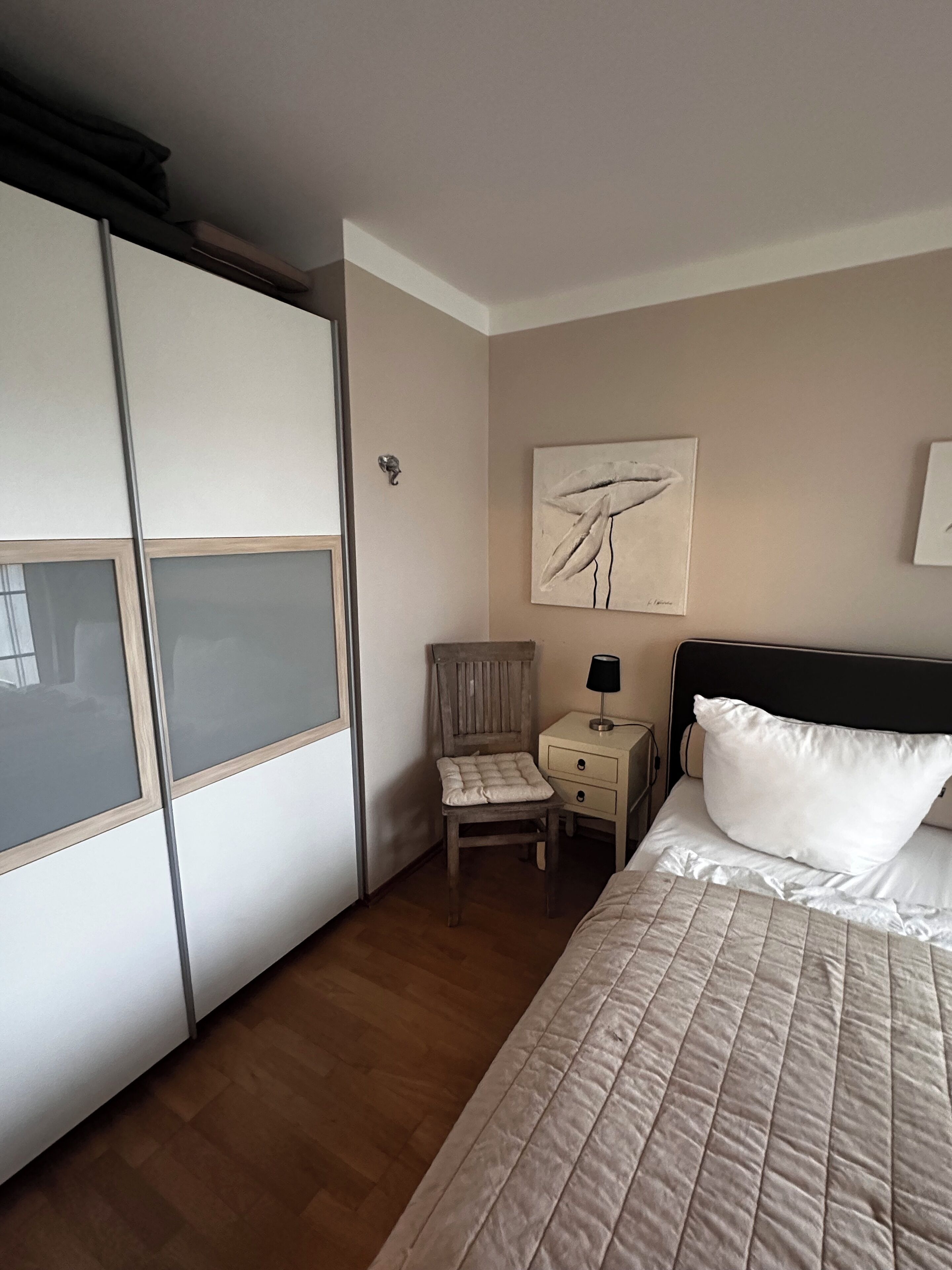 A hotel room with a bed, a chair, a nightstand, a wardrobe, and a painting on the wall.