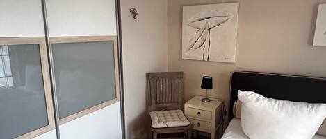 A hotel room with a bed, a chair, a nightstand, a wardrobe, and a painting on the wall.