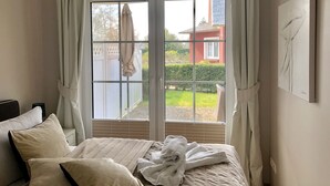 A bedroom with a large window, a bed with a white comforter, and a painting on the wall. - Exclusive apartment with garden and fireplace near the beach (Zingst)