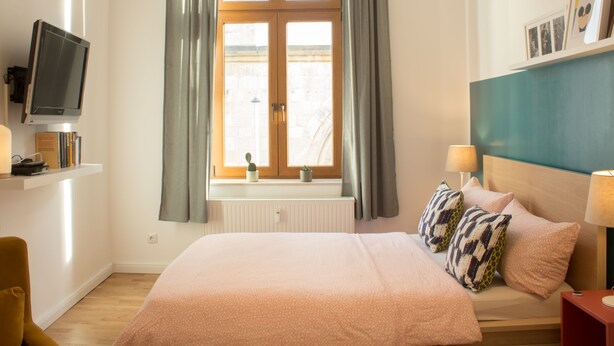 A bedroom with a bed, a television, a window with curtains, a radiator, and a bedside table with a lamp. - Apartment in the heart of Boppard (Boppard)