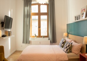 A bedroom with a bed, a television, a window with curtains, a radiator, and a bedside table with a lamp. - Apartment in the heart of Boppard (Boppard)