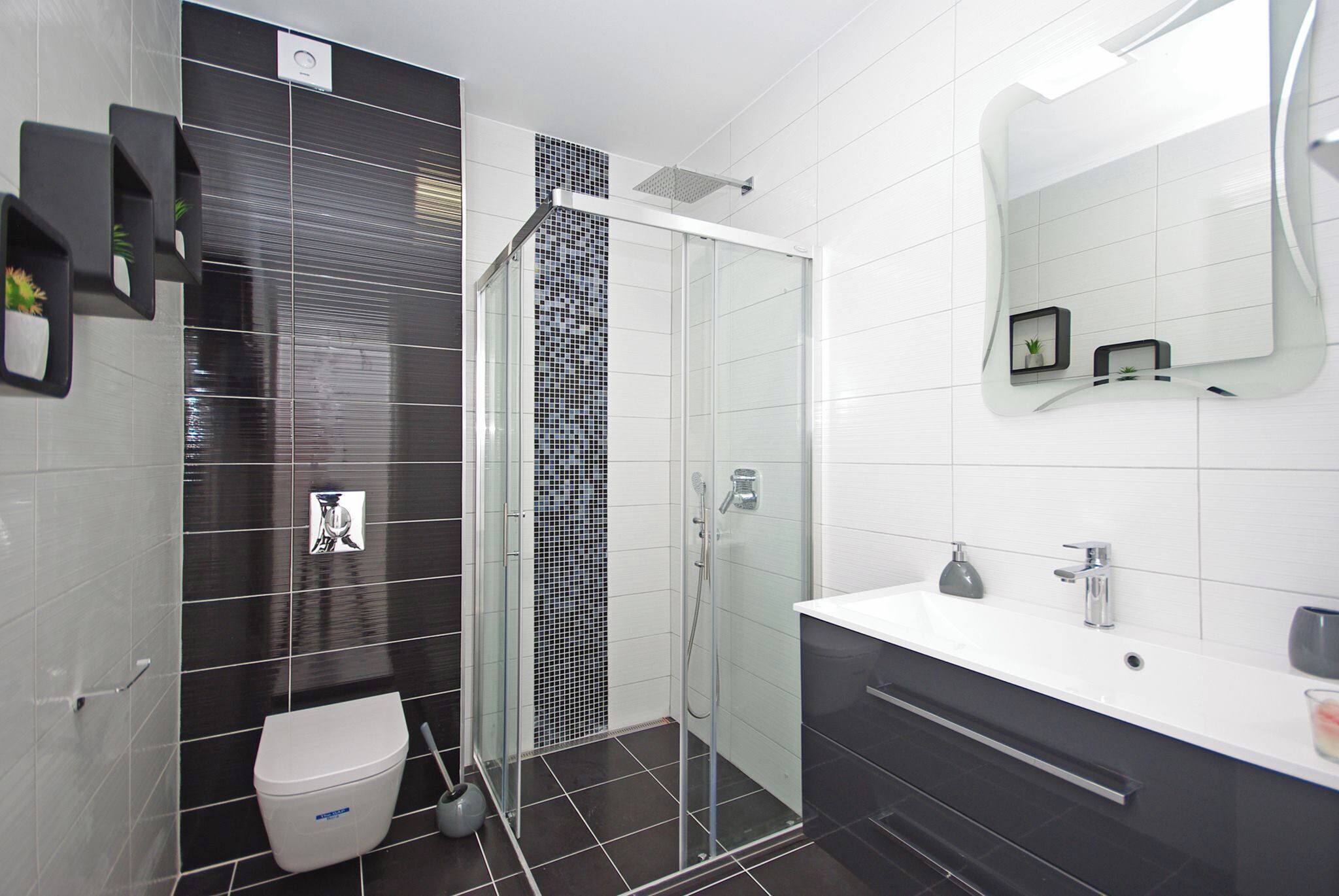 A modern bathroom with a glass-enclosed shower, a white sink, and a large mirror.