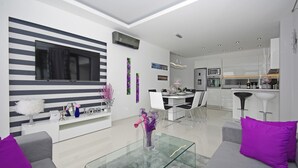 A modern living room with a glass coffee table, a sofa with purple cushions, a dining area with a white table and chairs, and a kitchen with modern appliances. - Modern Villa Nera with pool and sea view, three bedrooms 6+2 people (Makarska)