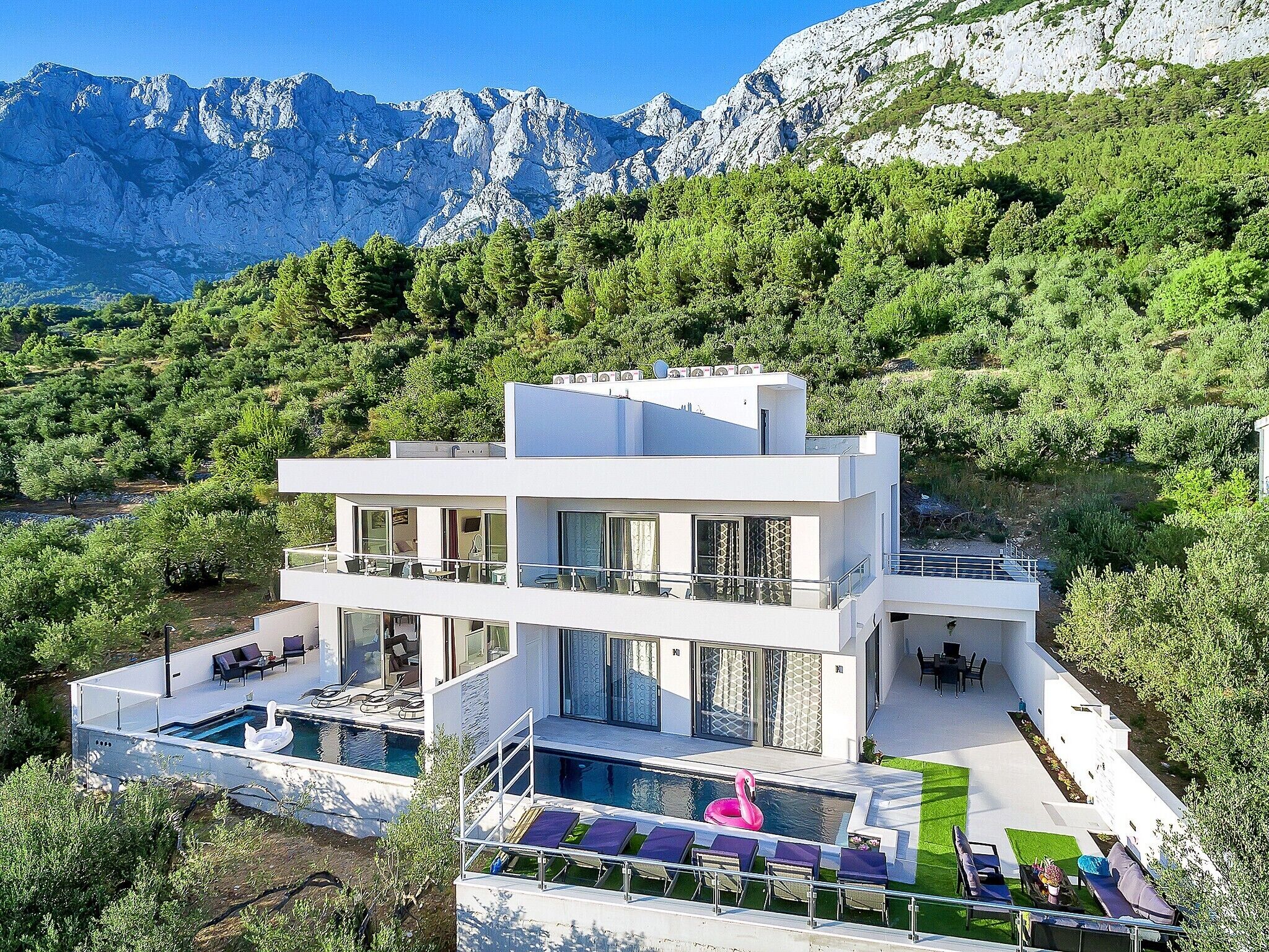 Un edificio moderno a due piani con piscina, area salotto esterna e vista sulle montagne.
