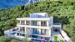A modern two-story building with a swimming pool, outdoor seating, and a view of mountains. - Modern Villa Nera with pool and sea view, three bedrooms 6+2 people (Makarska)