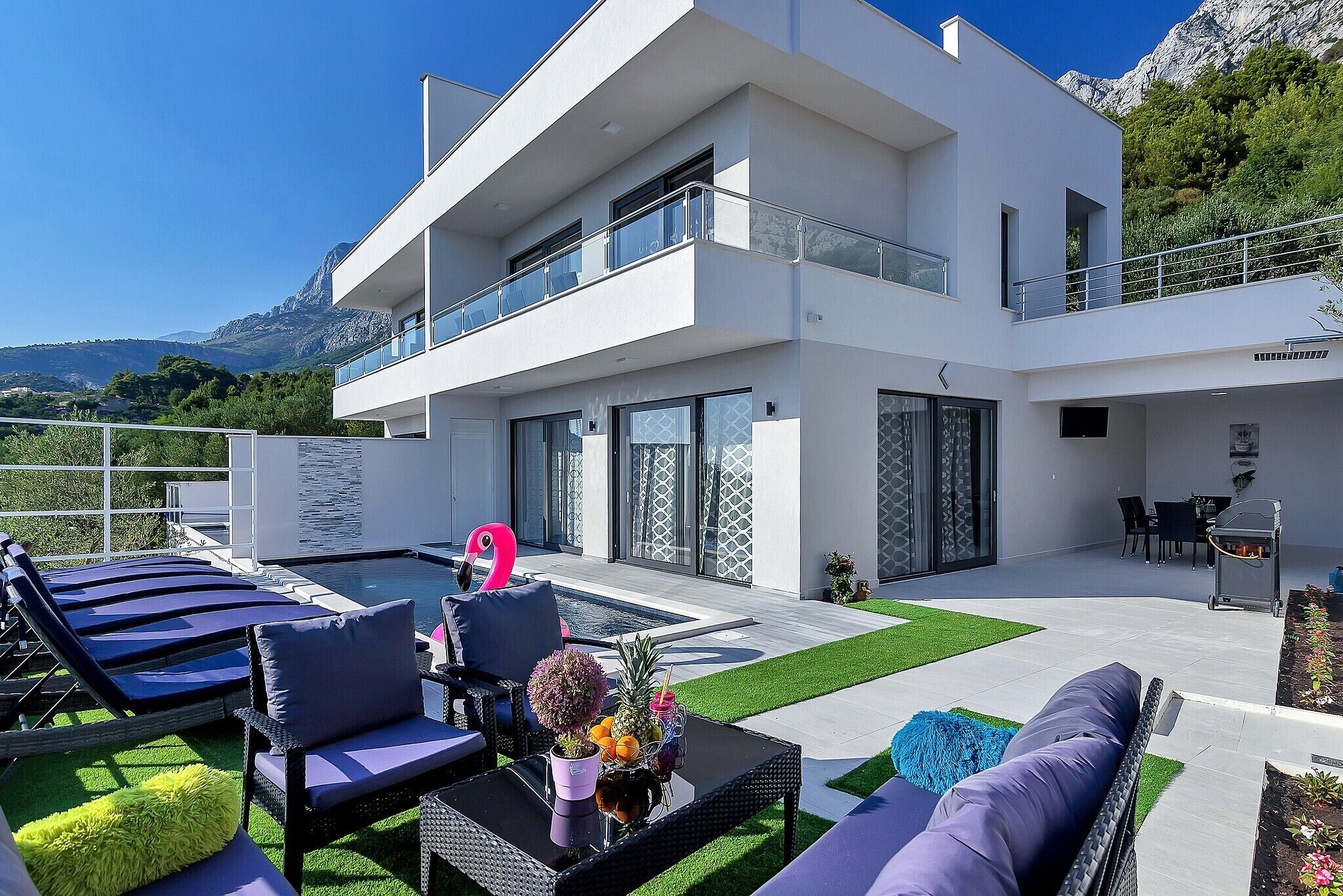 Una casa moderna de dos pisos con piscina, mobiliario exterior y vistas a montañas.