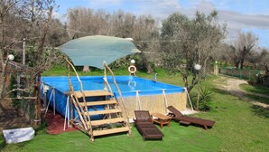 A swimming pool with a wooden deck and lounge chairs, surrounded by a grassy area and trees.