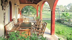 A covered patio with wooden furniture, a table, and arches.
