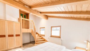 A bedroom with a wooden staircase, a bed, and a window.